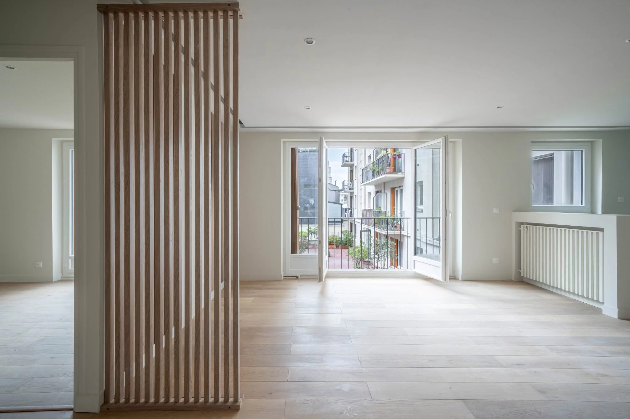 Séjour rénové avec parquet en chêne clair et claustra en bois ouvrant sur un balcon